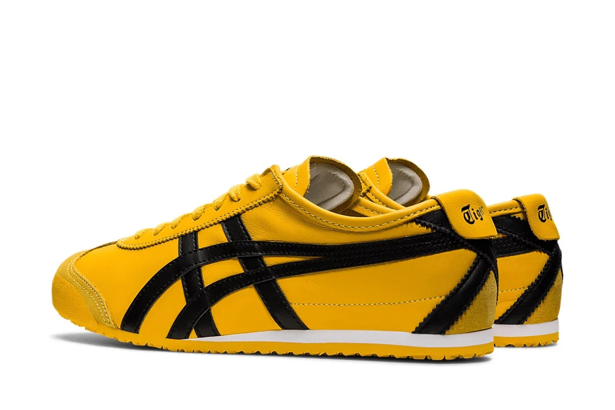 Tênis amarelo com detalhes pretos, estilo retrô, solado baixo e design esportivo clássico.