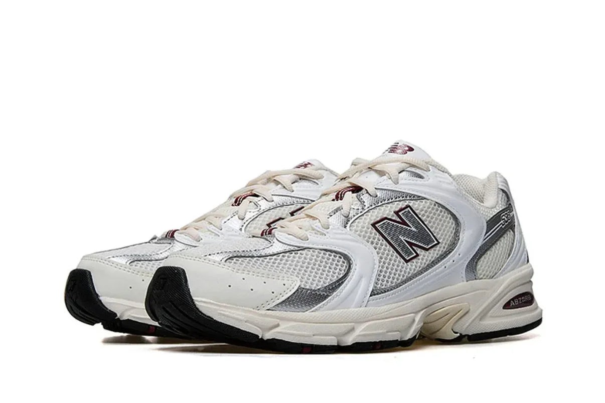 Tênis New Balance branco e cinza com detalhes em preto, design esportivo e solado robusto.