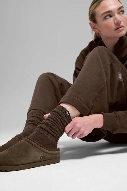 Modelo usando slipper marrom de camurça com calça de moletom e meia canelada, estilo casual