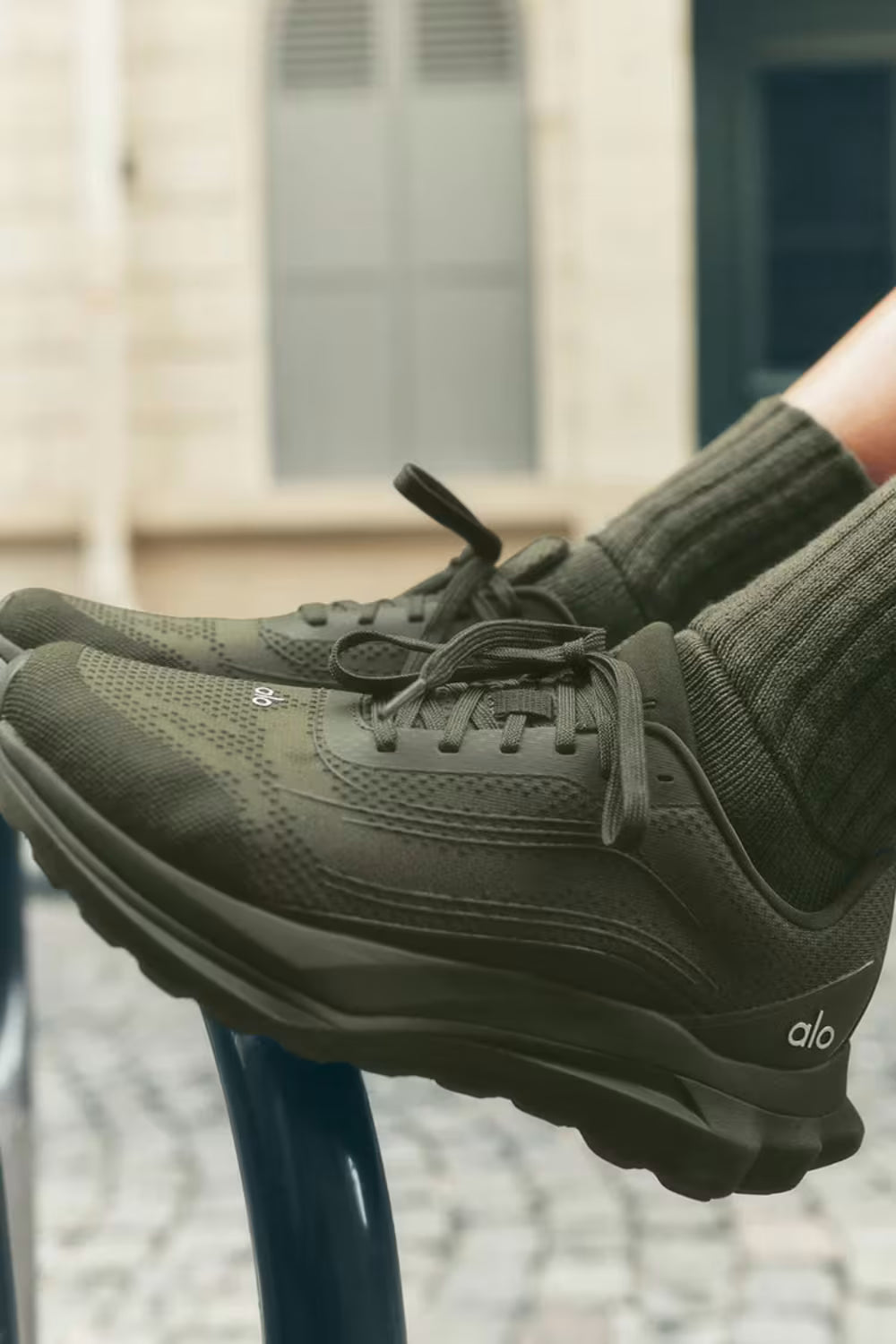 Tênis esportivo verde militar alo runner, solado robusto, usado em ambiente urbano.