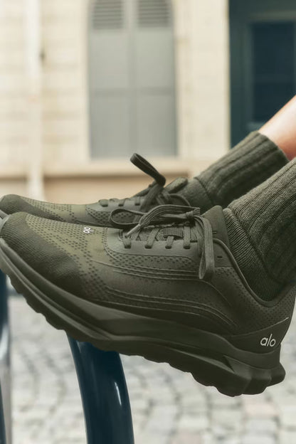 Tênis esportivo verde militar alo runner, solado robusto, usado em ambiente urbano.