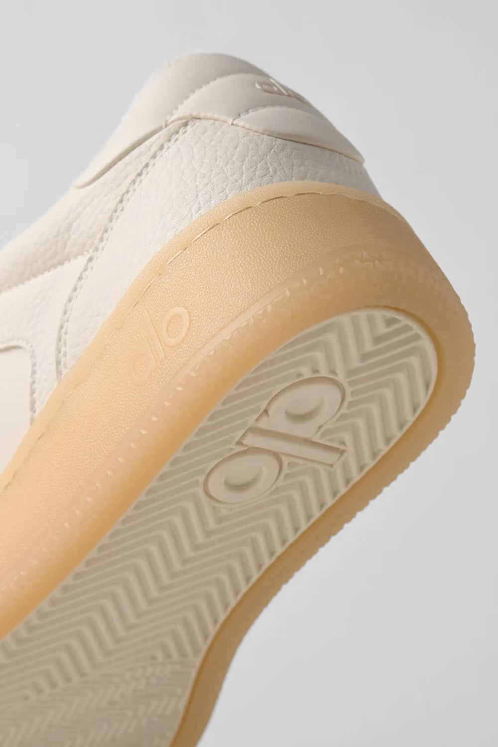 Detalhe do solado de um tênis bege com textura e logo em relevo, calçado esportivo premium.