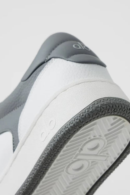 Detalhe traseiro de tênis esportivo cinza e branco com sola texturizada e logo visível.