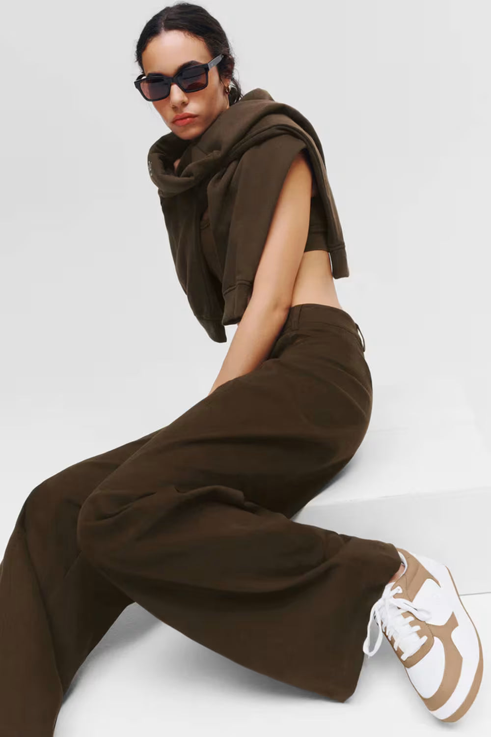 Modelo feminina vestindo conjunto marrom e tênis branco e marrom Alo Yoga em fundo claro