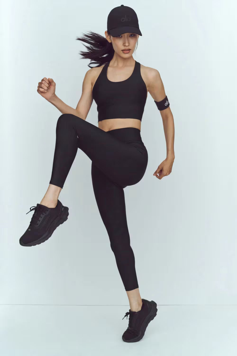 Modelo usando tênis de corrida preto, conjunto esportivo e boné, em pose atlética.