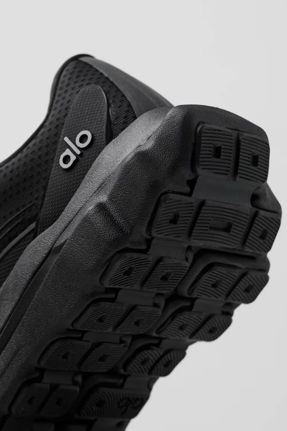 Tênis preto de corrida Alo Yoga, detalhe da sola robusta e traseira em foco.