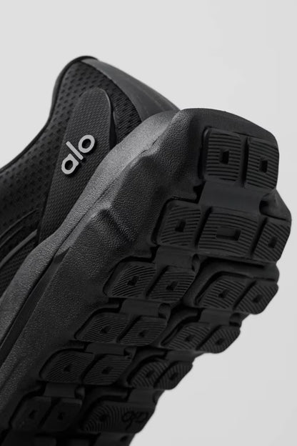 Tênis preto de corrida Alo Yoga, detalhe da sola robusta e traseira em foco.