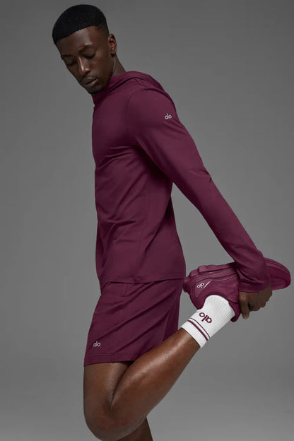 Homem vestindo conjunto esportivo vinho e tênis Alo Yoga Runner vinho, alongando perna.