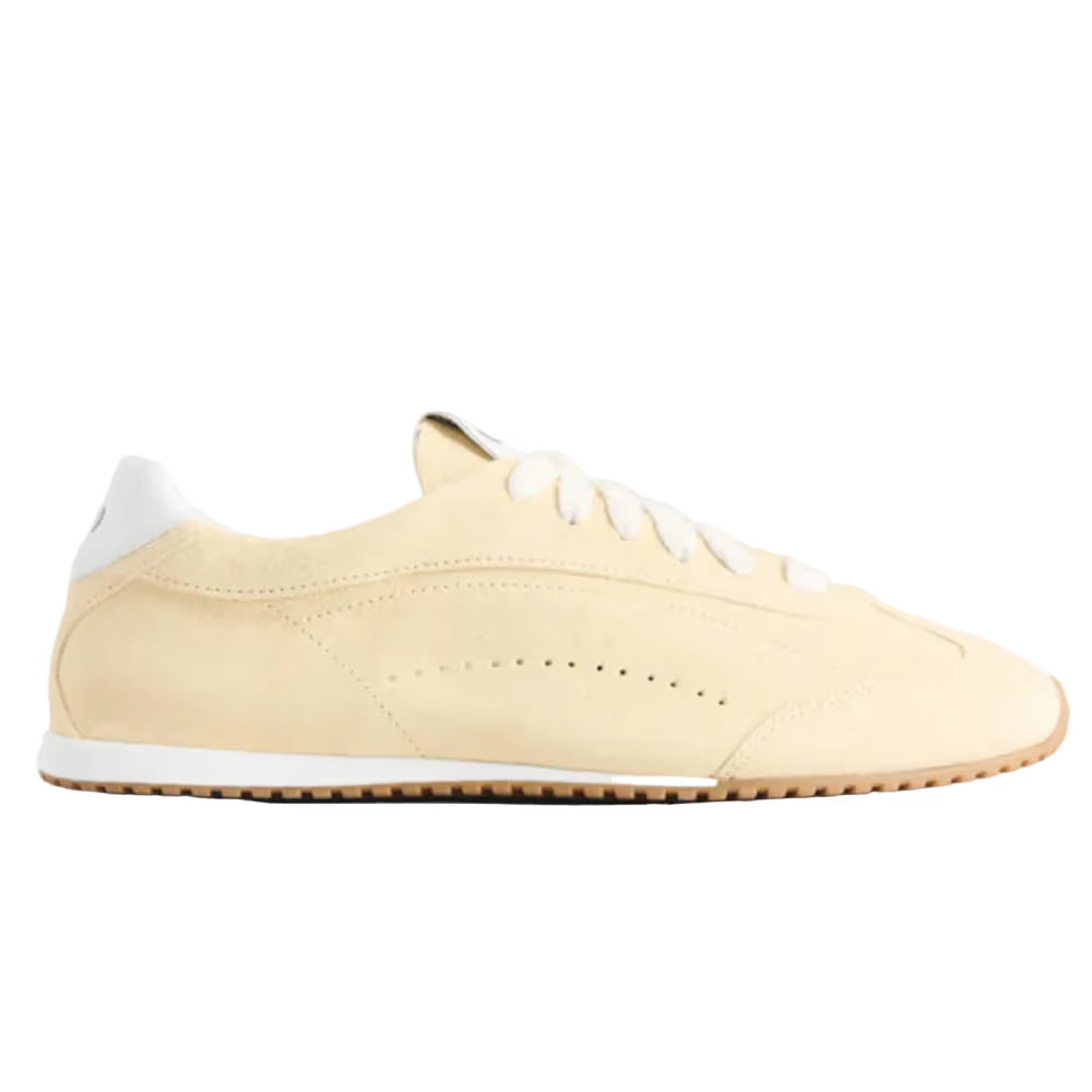 Tênis casual bege com detalhes dourados, solado baixo e cadarço branco, estilo minimalista.