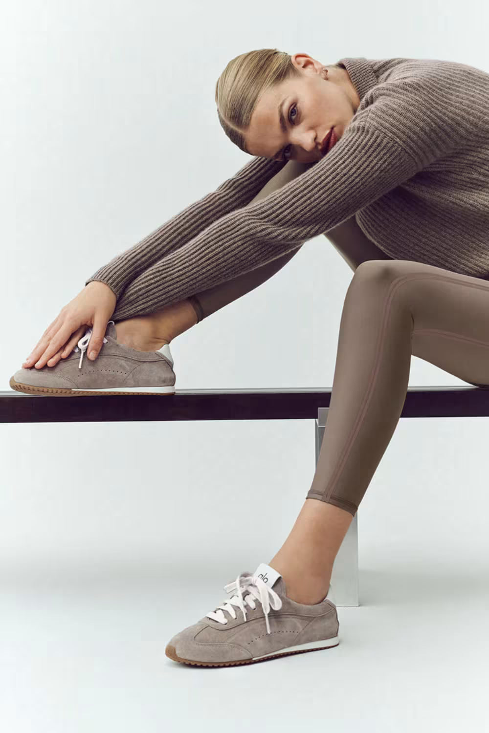 Mulher sentada usando tênis cinza Alo Yoga Sunset, look casual e moderno para o dia a dia.