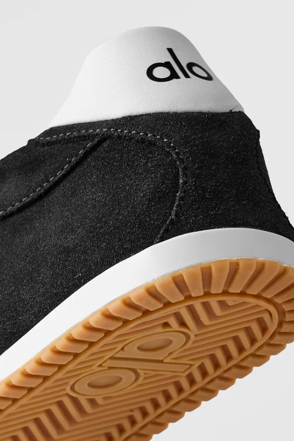Detalhe lateral e traseiro de tênis preto Alo Yoga, solado bege, design moderno.