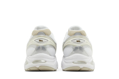 Tênis branco com detalhes bege e prata, sola robusta, vistos por trás, estilo esportivo moderno.