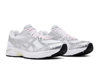 Tênis branco e prata estilo retrô, detalhes em mesh, solado robusto e cadarço rosa claro.