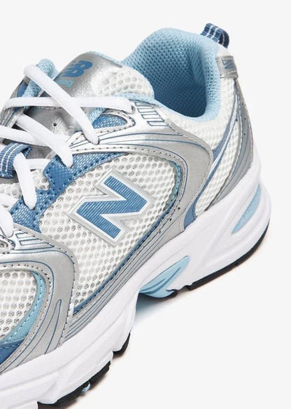 Tênis esportivo branco com detalhes prata e azul, cadarço branco, design moderno.