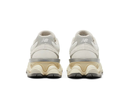Tênis branco New Balance 9060 vistos de trás, com solado robusto bege e cinza, detalhes em camurça.