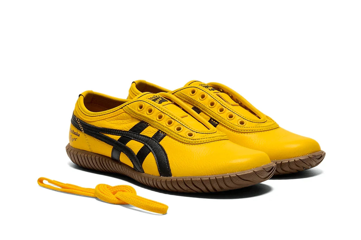 Tênis slip-on amarelo com detalhes pretos, solado marrom e cadarço amarelo ao lado