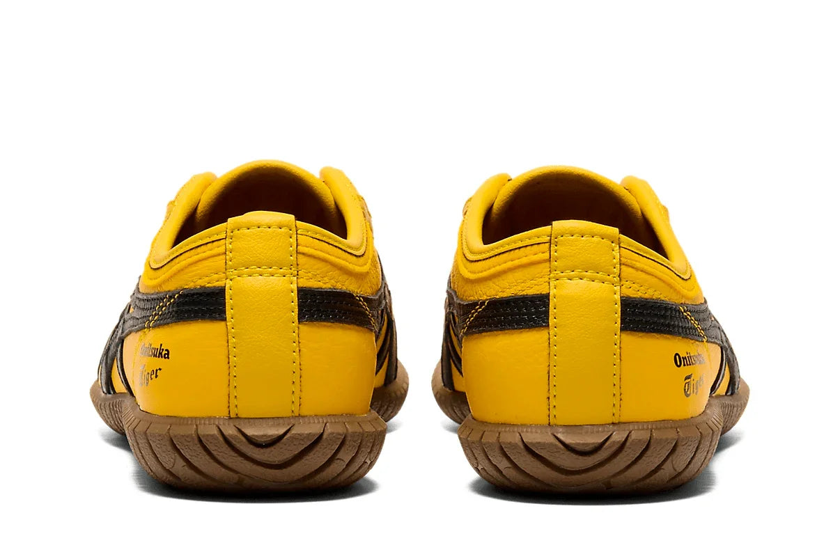 Tênis casual amarelo com detalhes pretos, solado marrom, visto de trás, estilo slip-on.