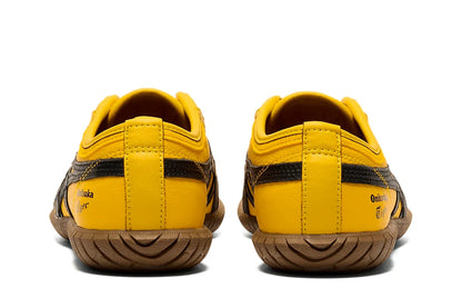 Tênis casual amarelo com detalhes pretos, solado marrom, visto de trás, estilo slip-on.